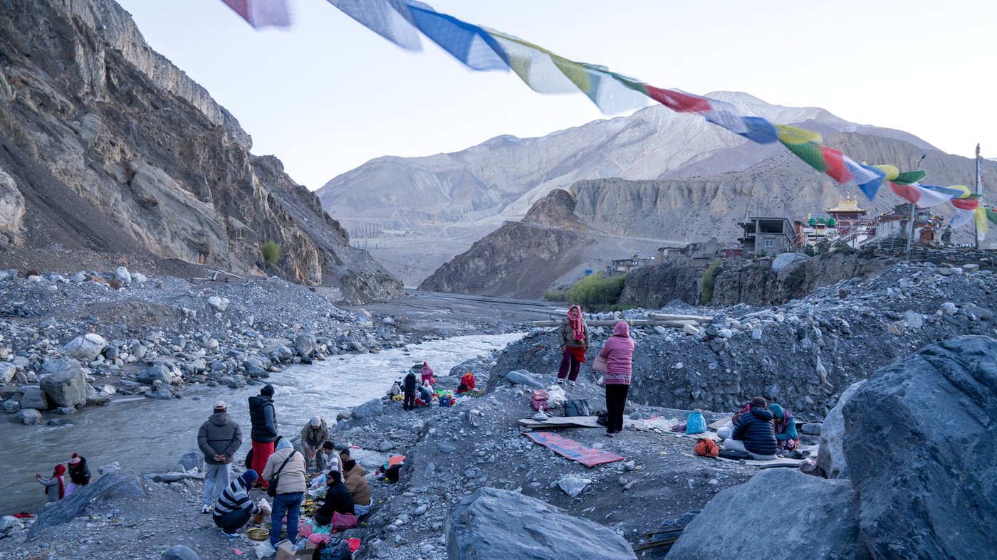 Community gathering by river with prayer flags, Nepal